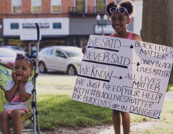 Two Smiling Black Children one holding Protest Sign explaining Black Lives Matter 