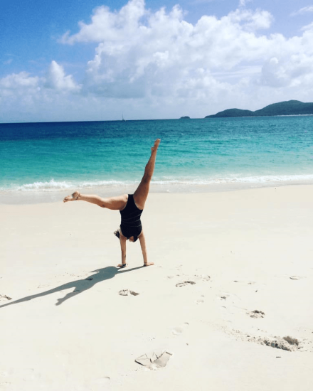 A picture of someone doing a cartwheel on a white sand beach with clear blue water in the background