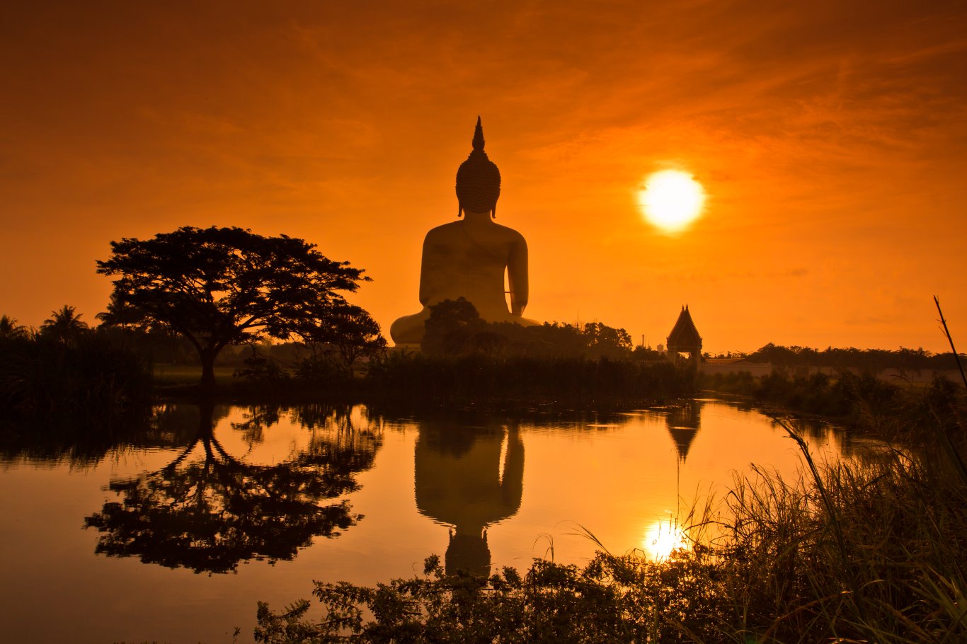 A scenic photo of a Buddha statue at sunset by a lake 