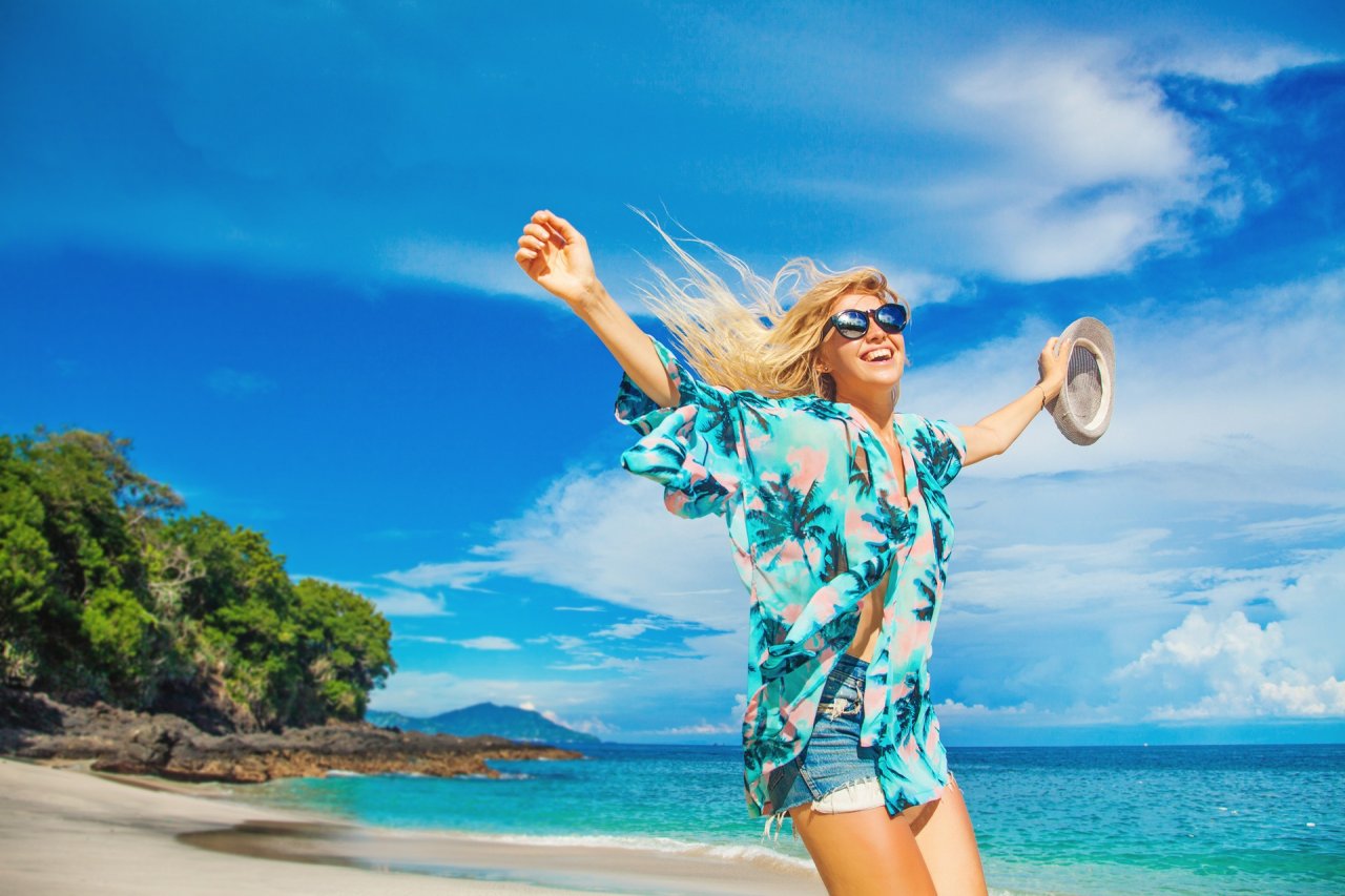 A girl wearing a blue floral shirt at the beach showing the clear blue sea and sky in the background