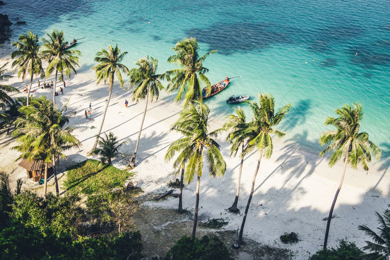 A view of a white sand beach, palm trees and clear blue ocean in the South of Thailand 