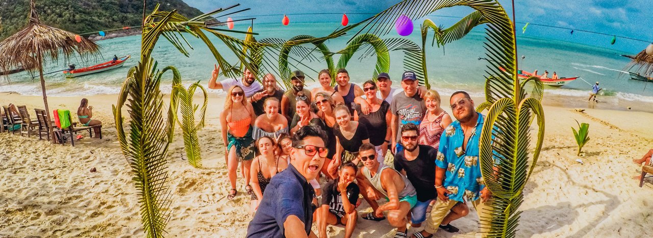 Group of Young Travellers on Bottle Beach Koh Phangan Thailand with colorful lights and Palm tree branches