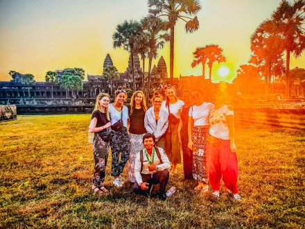 Group of Young Travellers in front of Angkor Wat Temple in Cambodia at Sunrise with Palm Trees