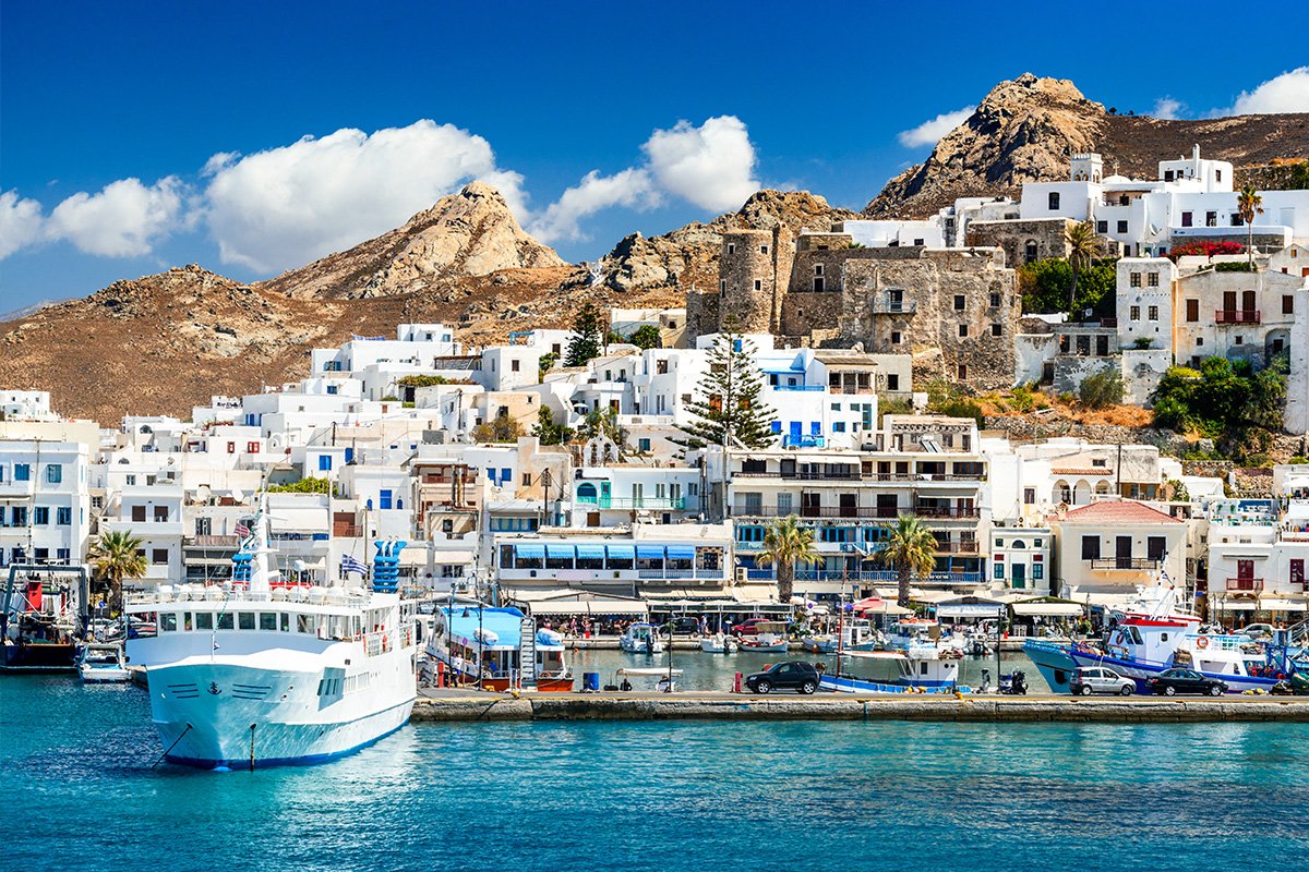 A view of the coast in Naxos Greece with white villas, the blue ocean and hills in view 