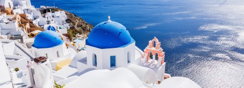 View of the tops of the white and blue villas in Santorini with the blue ocean in the background