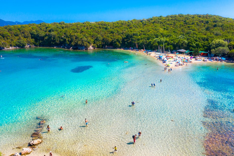 A scenic image of the blue lagoon in Syvota, Greece showing the crystal clear ocean, it's different shades of blue and the surrounding greenery