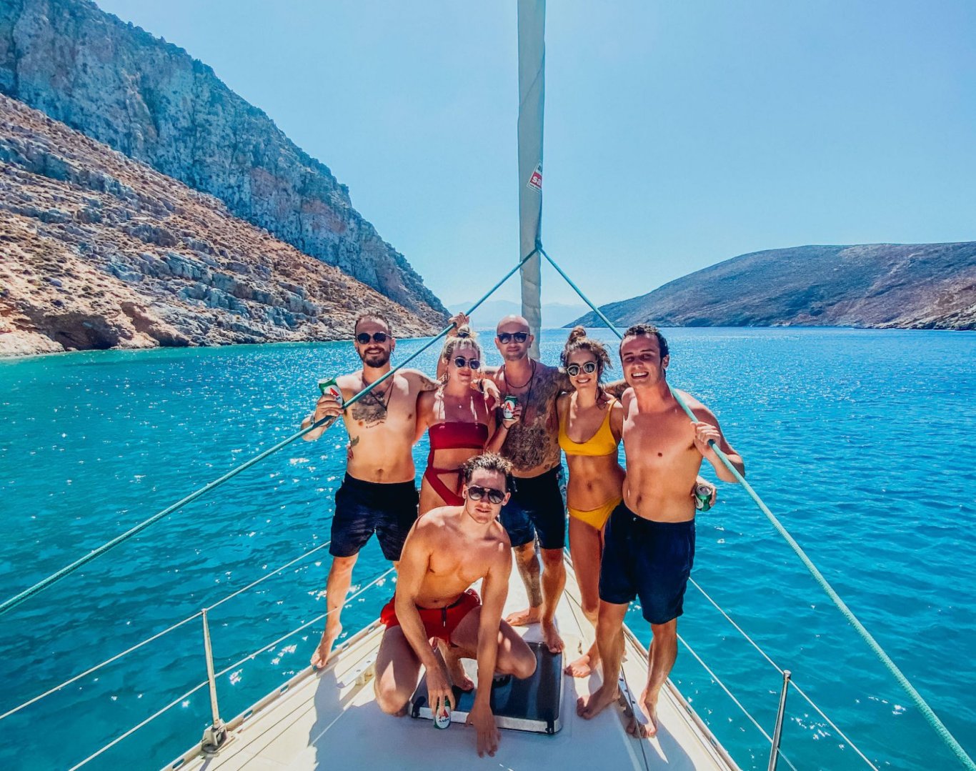 A group in swim wear on a sail boat in Corfu, Greece, surrounded by bright blue turquoise water and mountainous landscapes 