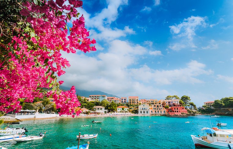 Beautiful coast of Kassiopi in Greece showing turquoise clear water, small boats  and a tree with magenta flowers 