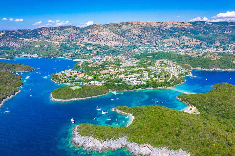 Aerial view of Syvota, Greece with different shades of blue in the sea, the town in the distance and lush green landscapes