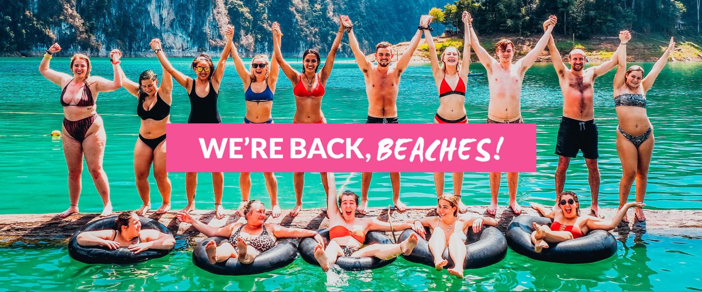 We're Back Beaches! Group of Young Travellers standing on floating Log Holding Hands in the air while others Float on Tubes in Lake