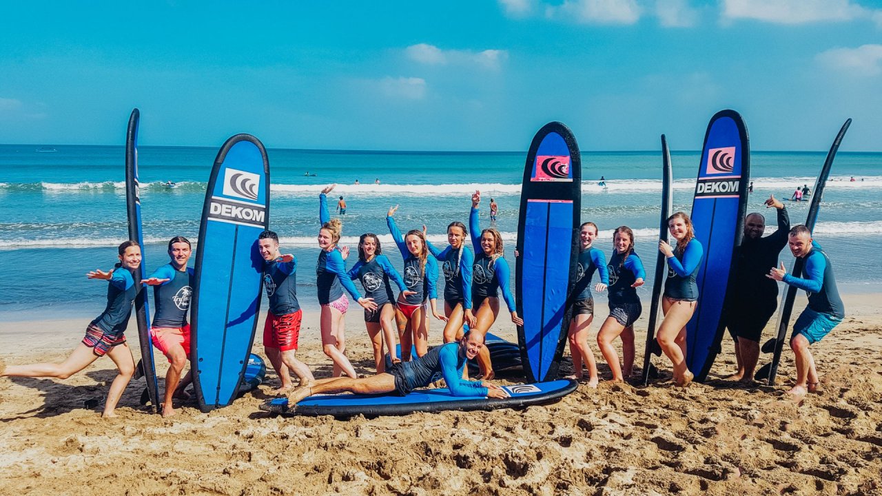 Group of travellers on beach with surf boards waving