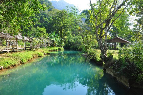 Bright blue river with green bank and trees with huts 