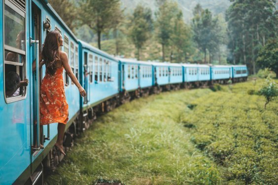 Girl in red dress leaning out of blue train in green countryside 