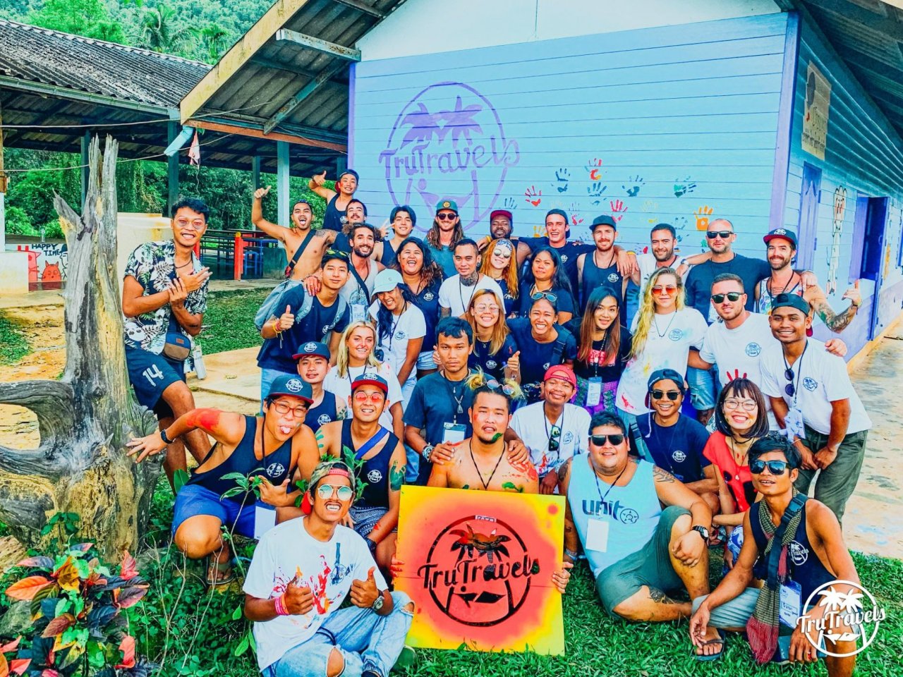 Group photo of TruCrew in front of blue building holding red and yellow TruTravels sign