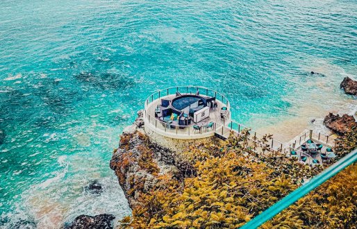 A stunning shot of a clifftop beach club in Bali, Indonesia showing the clearest bright blue sea and lush clifftops