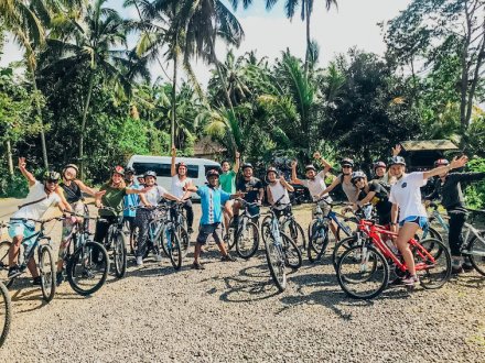 A group ready to go on a bike ride in Bali, Indonesia with lush greenery and palm trees in the background