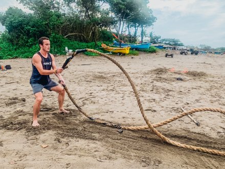 A guy using battle ropes on the beach in Bali, Indonesia during a HIIT workout