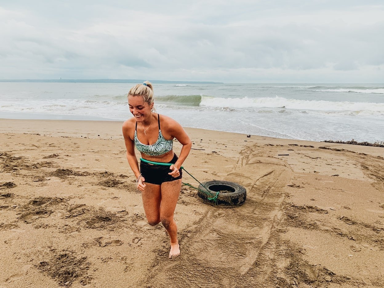 A girl pulling a car tyre on the beach during a HIIT workout in Bali, Indonesia 