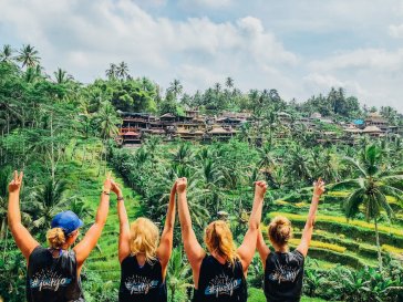 A group shot of four girls at the rice terraces in Ubud posing with their hands up, showing the lush green terraces in the background