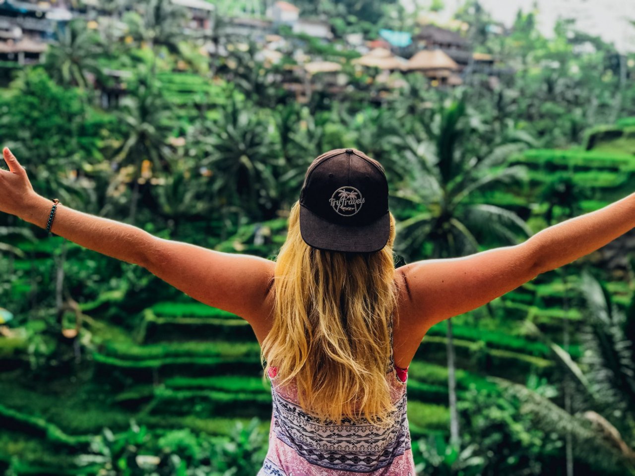 A girl posing with her arms out admiring the view of the emerald green rice terraces in Ubud, Bali, Indonesia