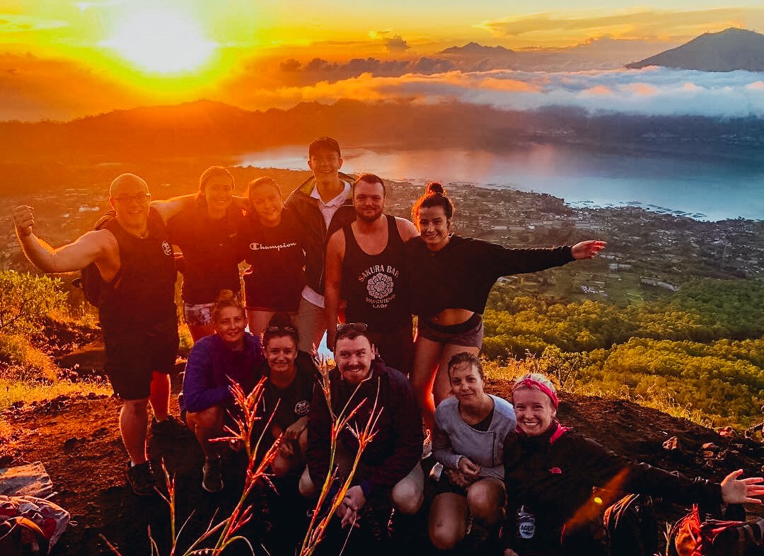 A group shot in front of the bright orange and golden sunrise while hiking Mount Batur in Bali, Indonesia 