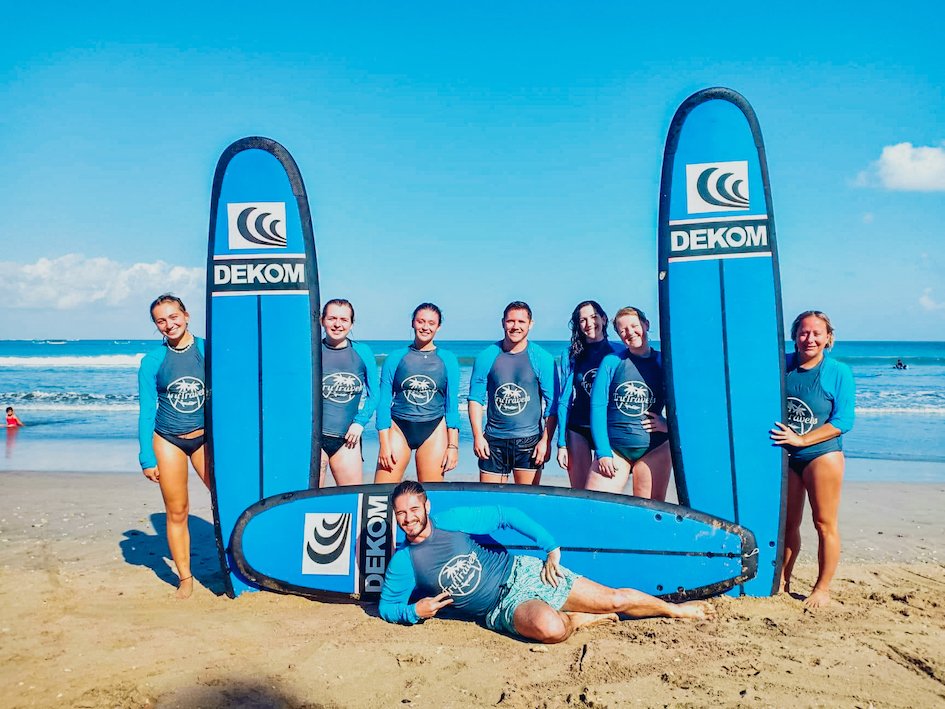 A group on the beach in Bali, Indonesia ready to surf with bright blue sky and sea in the background