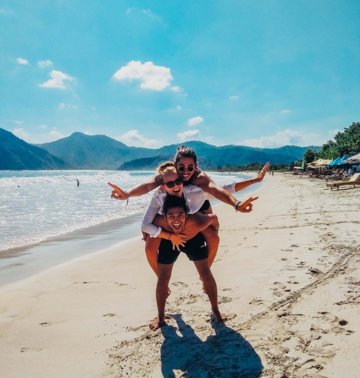 two girls on back of a guy on beach with blue sky