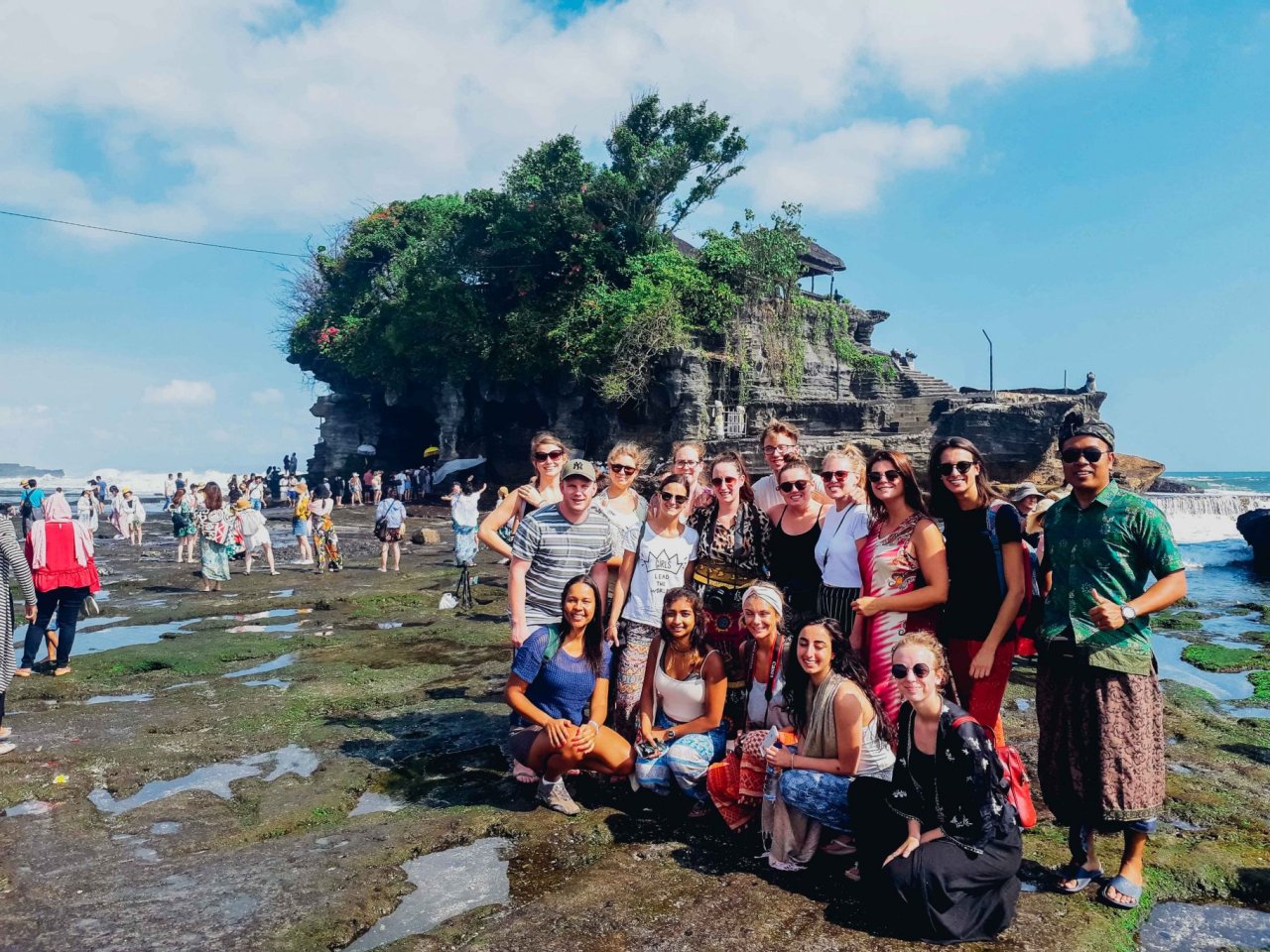 group of travellers standing in front of Tanah Lot temple in Bali