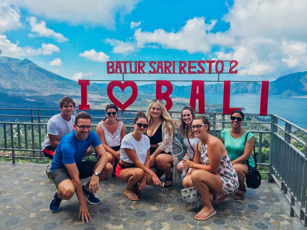I love Bali red sign with girls in front smiling and mountain backdrop