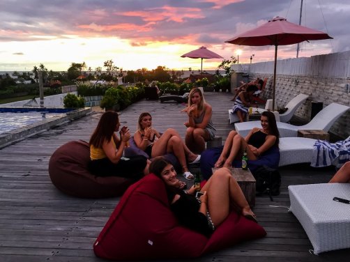group of girls sat on decking by rooftop pool with pink sunset in the background
