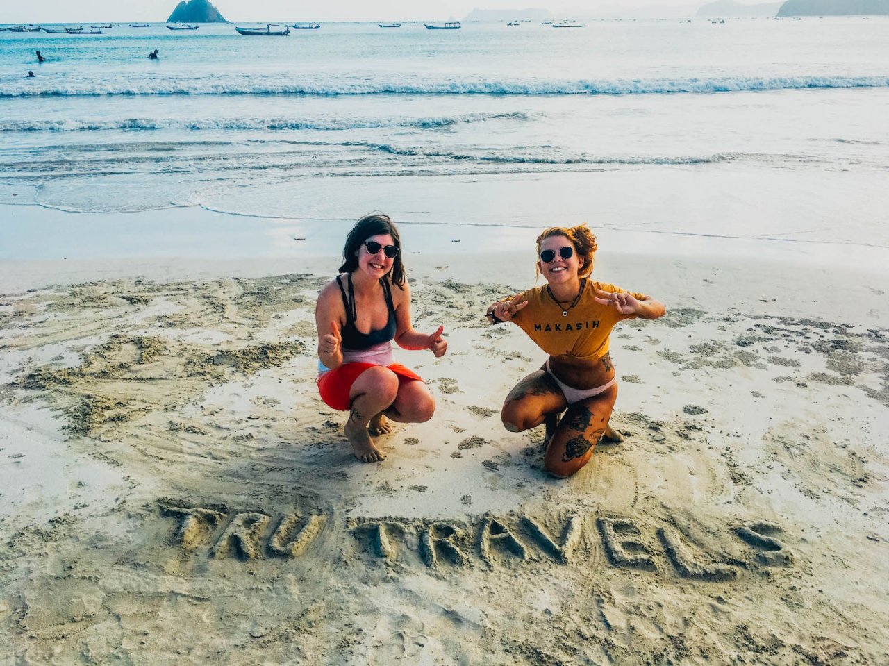 Two girls on a sandy beach in Bali, Indonesia with TruTravels carved into the sand 