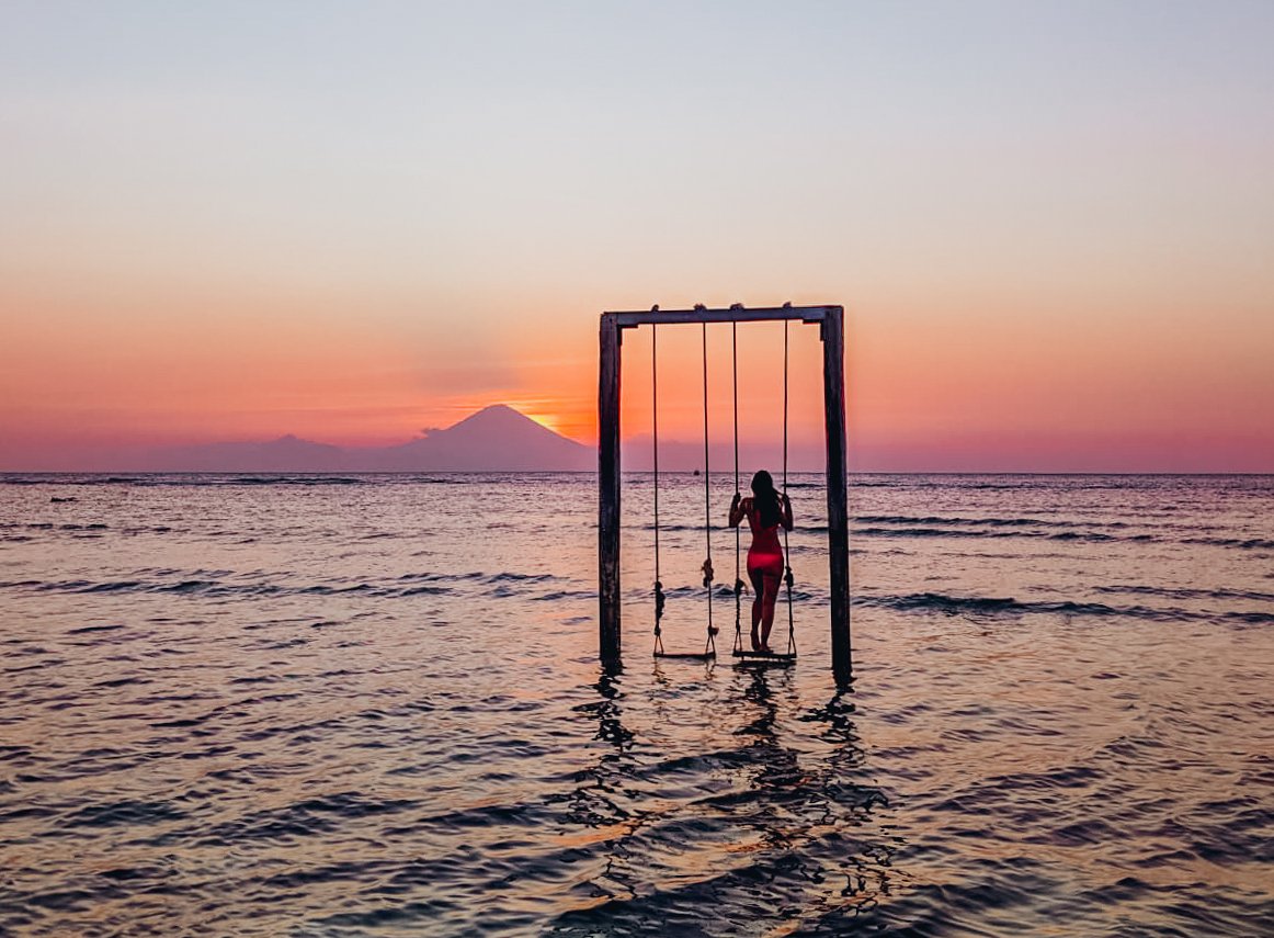 A girl on the famous swing in the sea watching the gorgeous pink sunset in Gili Trawangan Indonesia 