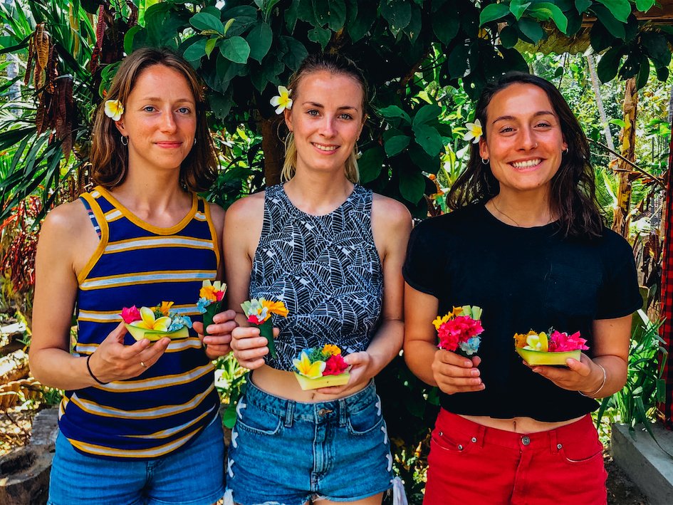 A group of 3 with flowers in their hair holding the canang sari offerings they made at traditional cooking class in Ubud, Bali, Indonesia 