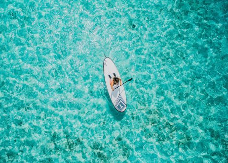 A birds eye view shot of someone on a paddle board in the middle of the glistening clear water in the Maldives 