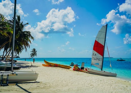 A scenic photo of small sail boats on the beach in the Maldives with the ocean and blue sky in the background