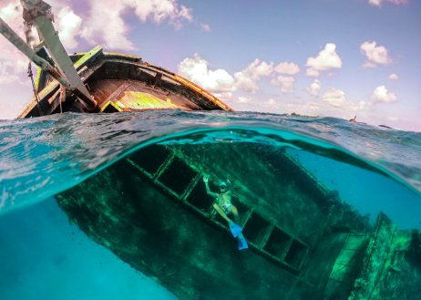 A split-shot of someone snorkelling around the ship wreck in the clear blue water in the Maldives 