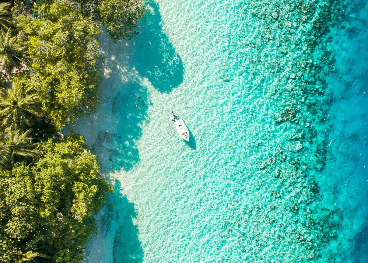 An aerial shot of the sailing boat on the bright blue clear water with luscious greenery in view in the Maldives 