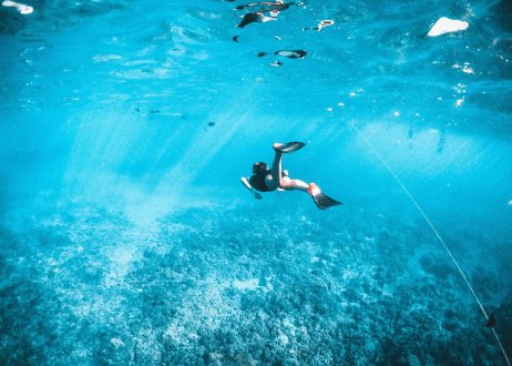 An underwater shot of someone snorkelling in the bright blue sea in the Maldives