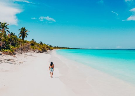 A picturesque photo of someone walking along a white sand pristine beach showing the bright crystal clear ocean in the Maldives 