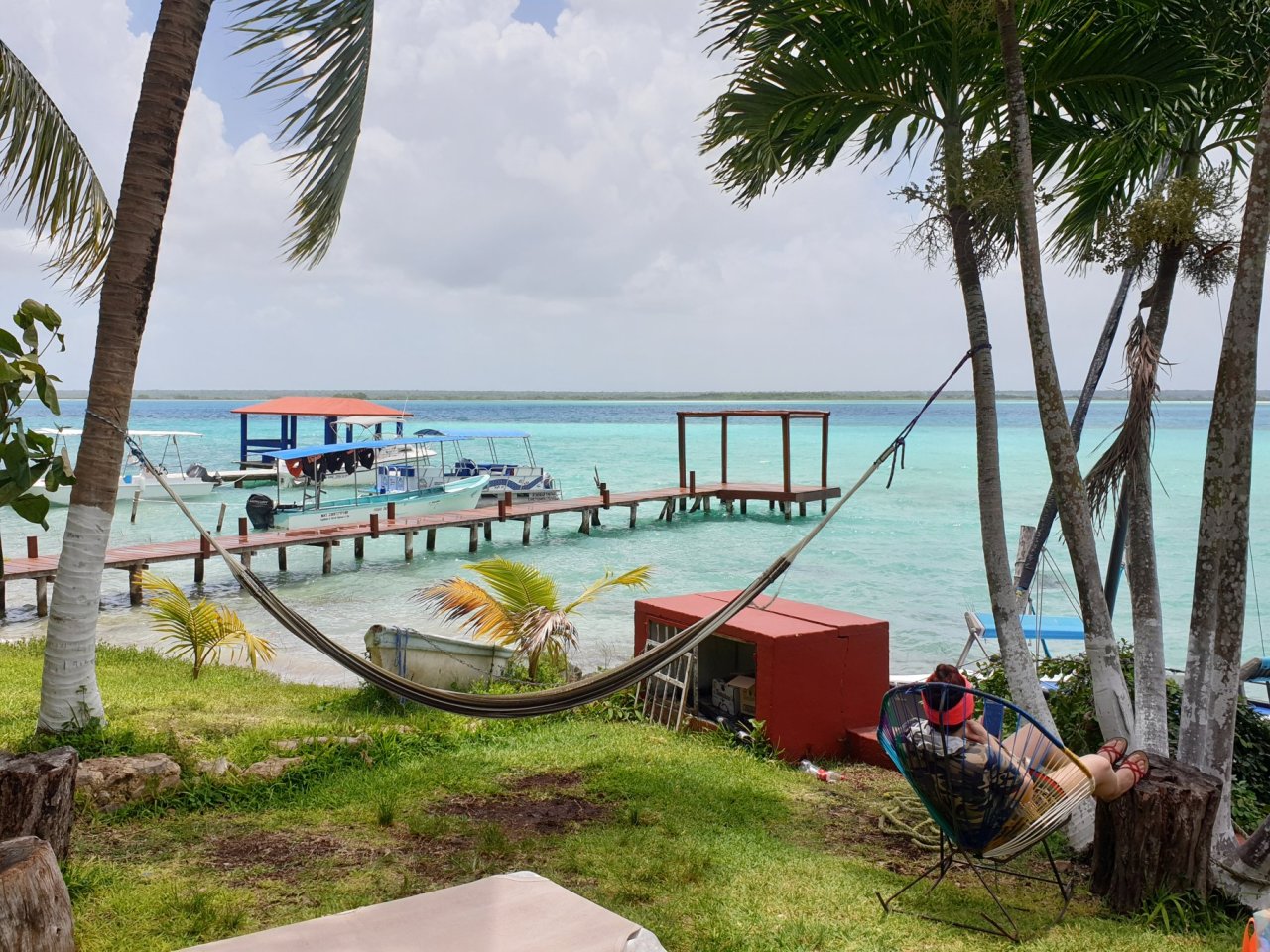 A scenic view of the waterfront in Mexico, showing a hammock, a jetty and bright blue water 