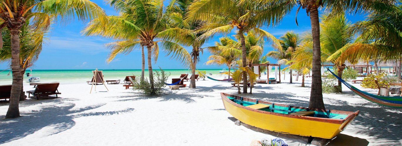 A shot of a white sand beach, palm trees and the bright blue ocean in the background with a small yellow boat on the sand in view