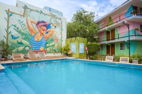A shot of the pool at the 1st hotel in Mexico showing a mural on a wall and colourful buildings 