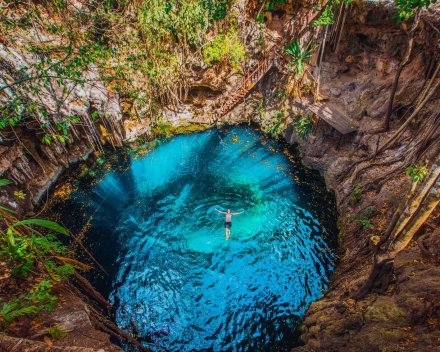 An aerial view of someone swimming in a bright clear blue Cenote in Mexico 
