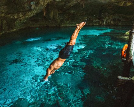 A guy diving into a bright blue clear water Cenote in Mexico 