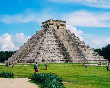 A picturesque shot of the Mayan Ruins of Chichen Itza in Mexico, showing blue sky and bright green grass. 