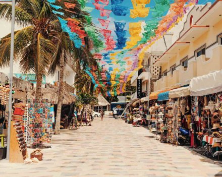 A shot of a street in Playa Del Carmen, Mexico, with colourful flags, palm trees and surrounding market stalls.