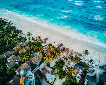 A scenic shot of the coast in Tulum, Mexico, showing the bright blue clear sea, white sandy beach and surrounded beach houses 