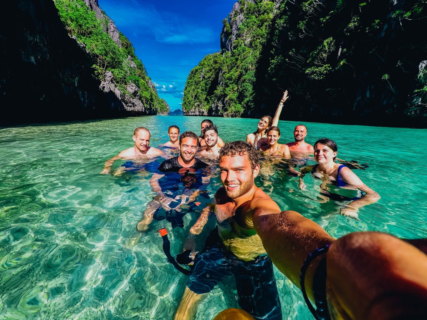 Group of travelling in clear blue sea, surrounded by islands smiling at camera 