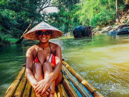 A girl on a bamboo raft trip with an elephant in the background bathing in the river in Chiang Mai Thailand