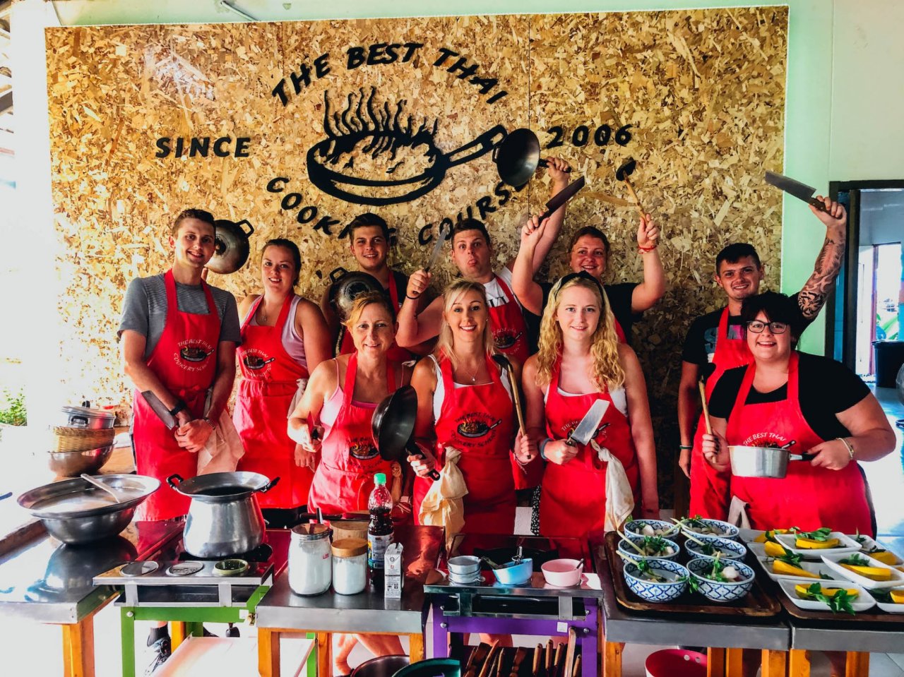 A group photo at the cooking class in Chiang Mai holding all the cooking utensils